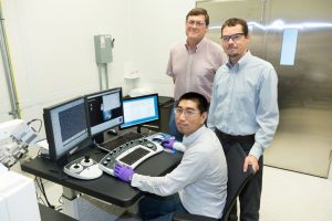 Yang Song da ORNL (sentada), Dale Hensley (de pé à esquerda) e Adam Rondinone examinam uma amostra de nanospike de carbono com um microscópio eletrônico de varredura.